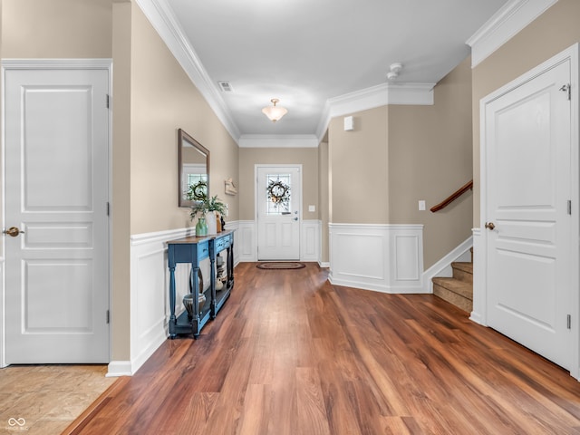 foyer entrance featuring stairway, visible vents, ornamental molding, wood finished floors, and wainscoting