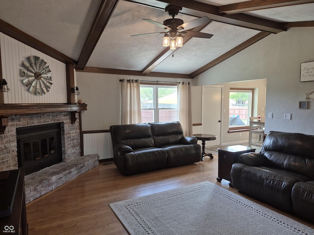 living area with vaulted ceiling with beams, a ceiling fan, wood finished floors, and a brick fireplace
