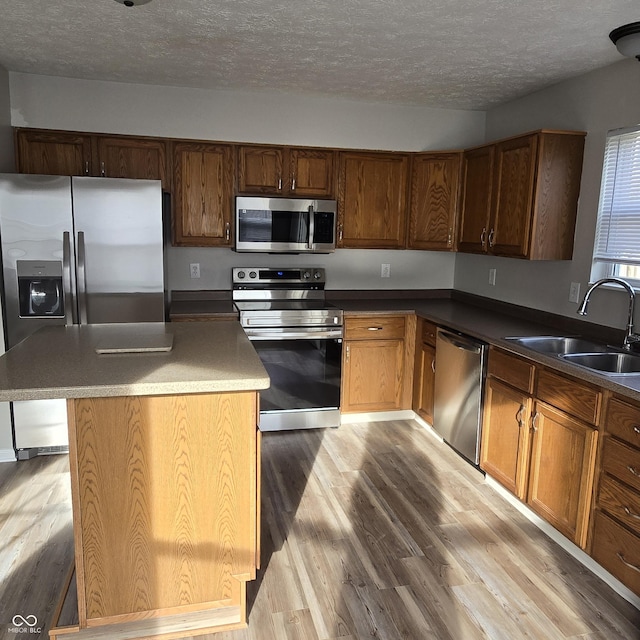 kitchen with light wood-style flooring, appliances with stainless steel finishes, brown cabinets, a sink, and a textured ceiling