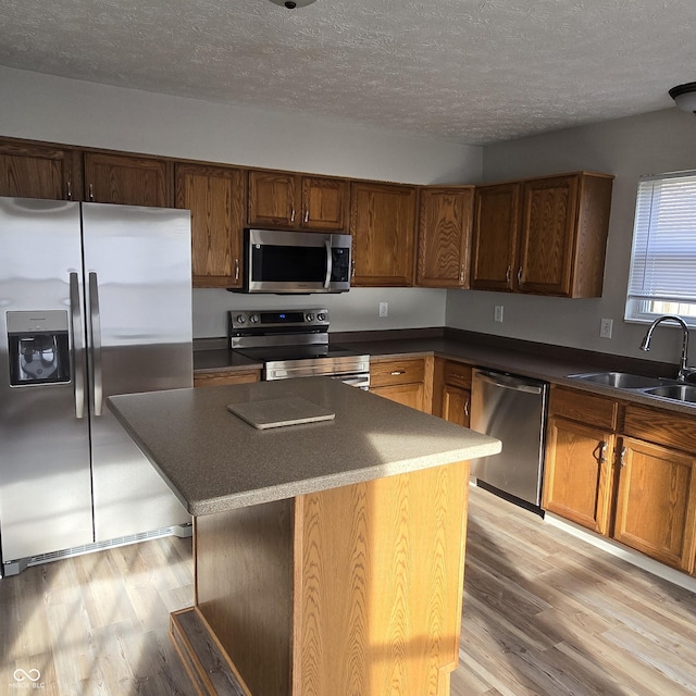 kitchen with light wood-style flooring, stainless steel appliances, a kitchen island, a sink, and a textured ceiling