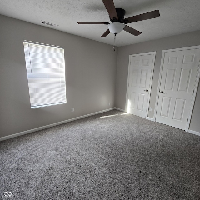 unfurnished bedroom featuring carpet flooring, ceiling fan, visible vents, baseboards, and a textured ceiling