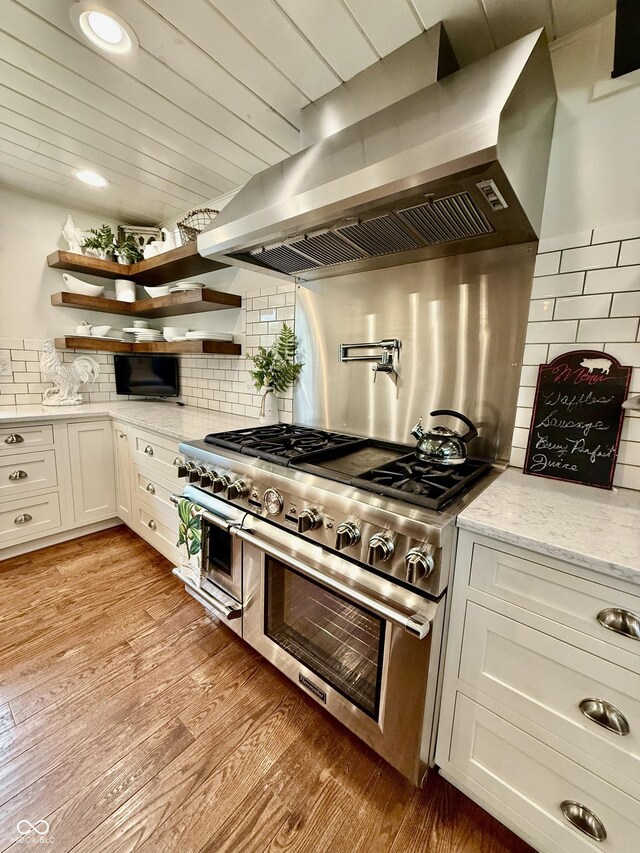 kitchen featuring light stone countertops, tasteful backsplash, wall chimney exhaust hood, double oven range, and white cabinets