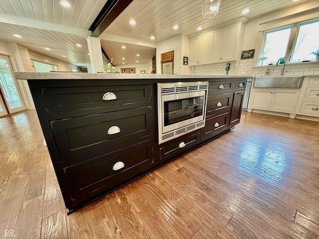 kitchen with stainless steel microwave, light wood-style flooring, white cabinetry, and a sink