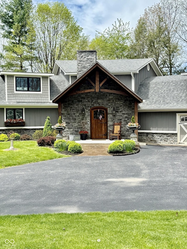 view of front of home with a chimney, stone siding, board and batten siding, and a shingled roof
