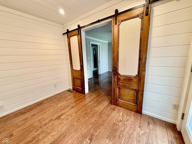 unfurnished room with a barn door, baseboards, wooden walls, light wood-type flooring, and recessed lighting