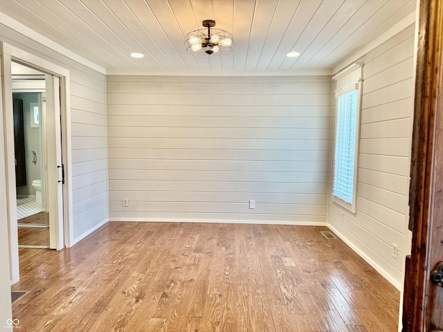 unfurnished dining area featuring wood ceiling, light wood-style floors, visible vents, wooden walls, and a wealth of natural light