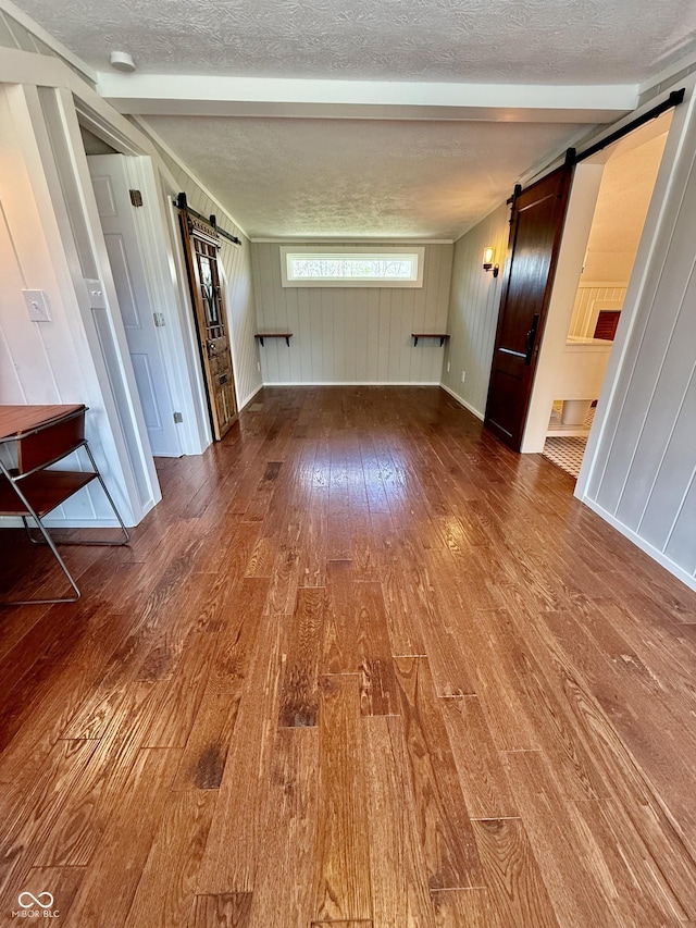 unfurnished living room featuring beam ceiling, a barn door, a textured ceiling, and wood-type flooring