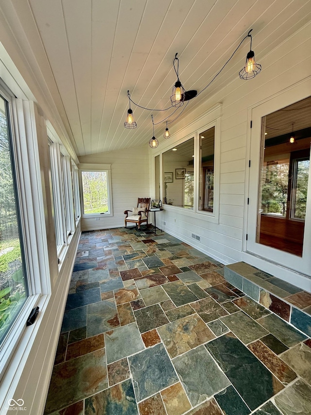 unfurnished sunroom with stone tile floors, wood walls, and visible vents