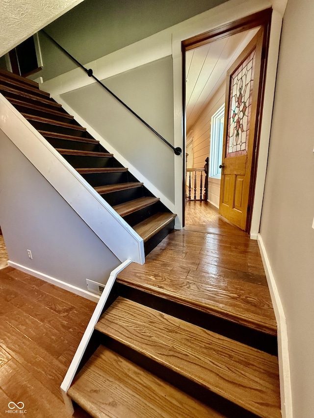 staircase featuring lofted ceiling, hardwood / wood-style floors, and baseboards