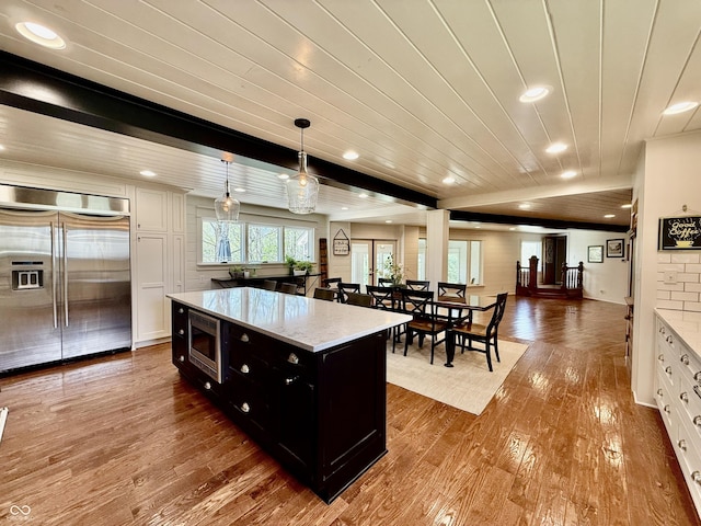 kitchen with built in appliances, wood finished floors, dark cabinets, and open floor plan