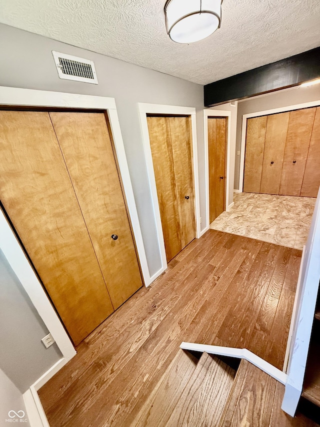 unfurnished bedroom with visible vents, hardwood / wood-style flooring, a textured ceiling, and multiple closets