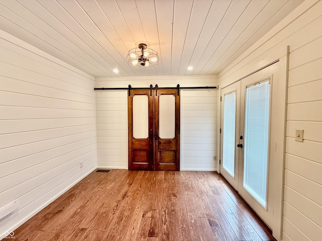entrance foyer featuring wood walls, wood finished floors, a barn door, and french doors