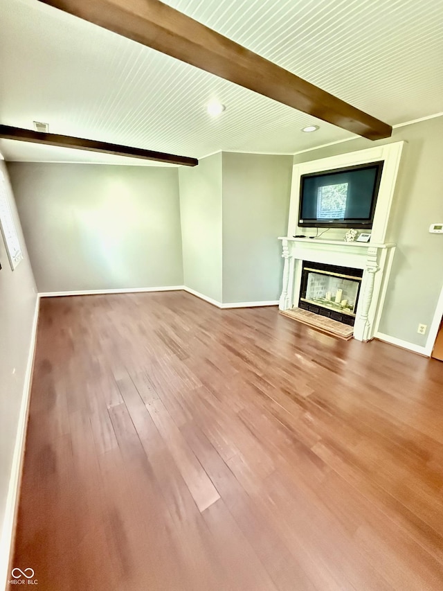 unfurnished living room featuring beamed ceiling, baseboards, wood finished floors, and a glass covered fireplace