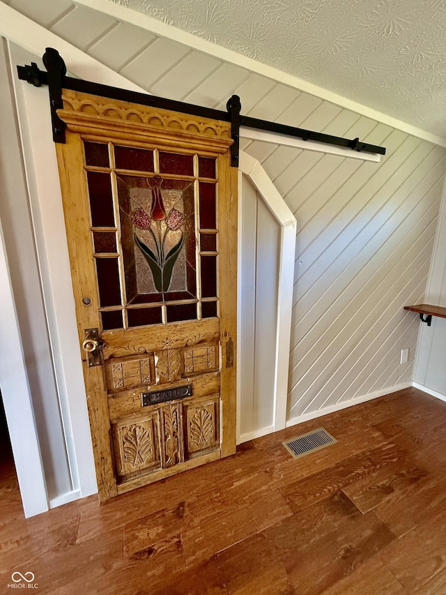 interior details with visible vents, a barn door, wood finished floors, and beam ceiling