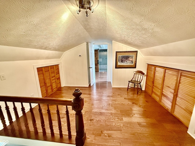 additional living space with lofted ceiling, a textured ceiling, wood finished floors, and baseboards