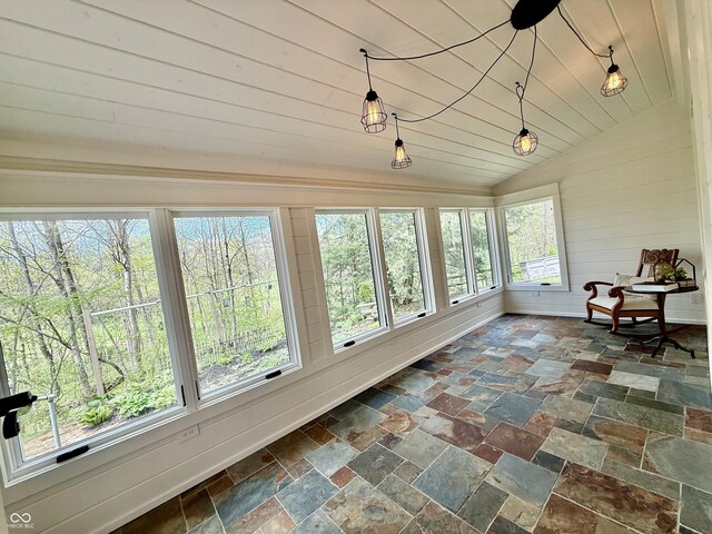 sunroom / solarium with stone tile floors, wooden walls, and vaulted ceiling