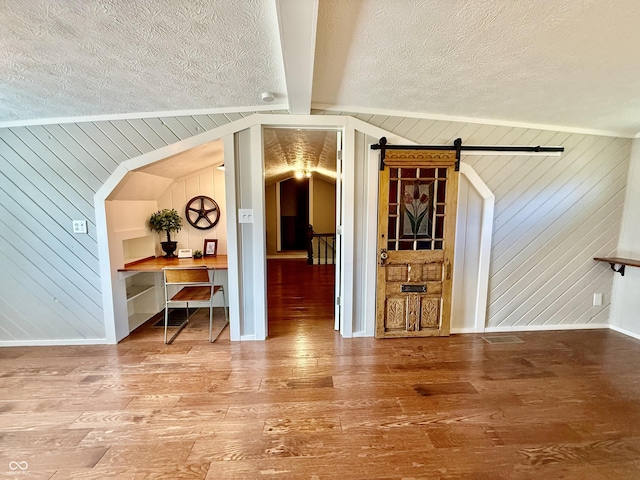 interior space with wood-type flooring, a textured ceiling, wooden walls, and a barn door