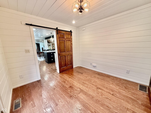 empty room featuring wood walls, a barn door, visible vents, and light wood-style floors