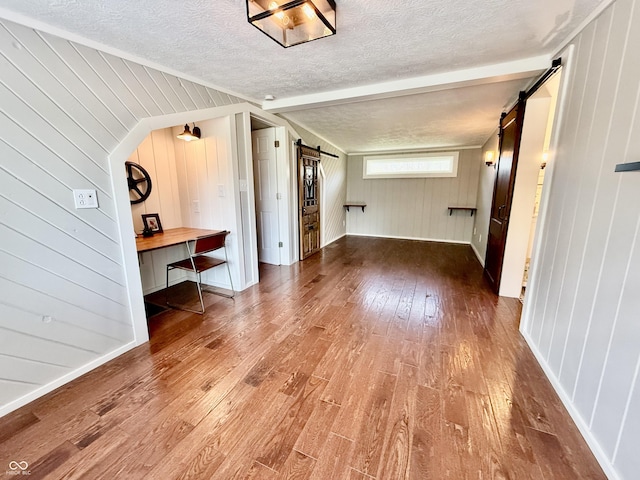 additional living space featuring hardwood / wood-style flooring, wood walls, a barn door, and a textured ceiling