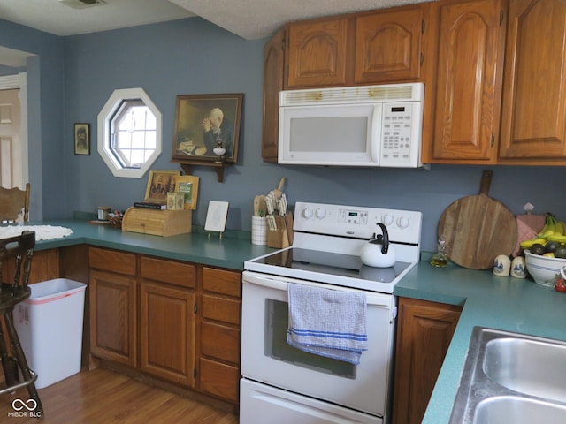 kitchen featuring visible vents, white appliances, brown cabinetry, a sink, and light wood-type flooring