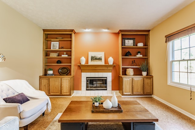 living room with a textured ceiling, a tiled fireplace, built in features, baseboards, and carpet flooring