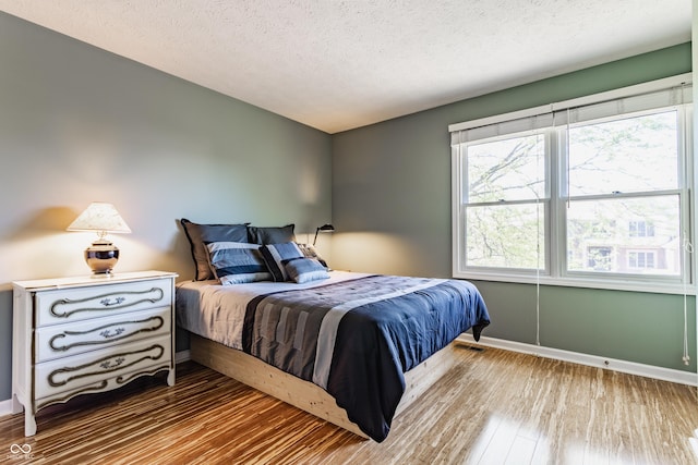 bedroom with baseboards, a textured ceiling, wood finished floors, and multiple windows