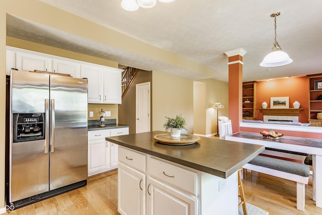 kitchen featuring dark countertops, stainless steel fridge, light wood finished floors, white cabinetry, and open floor plan
