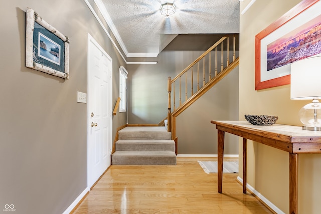 foyer entrance with light wood-style floors, ornamental molding, a textured ceiling, and stairway