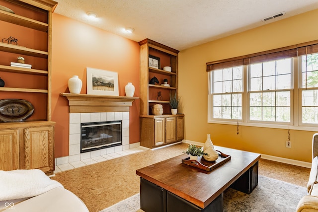 carpeted living room with a textured ceiling, a tiled fireplace, built in features, baseboards, and visible vents
