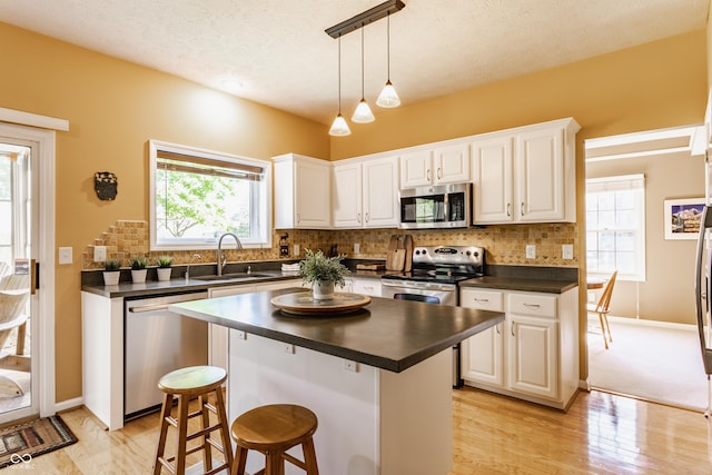 kitchen featuring dark countertops, appliances with stainless steel finishes, a sink, and light wood-style floors