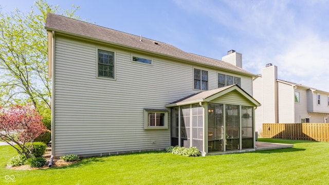 rear view of house with a yard, fence, a chimney, and a sunroom