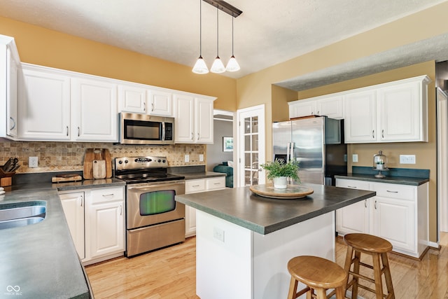 kitchen with white cabinets, dark countertops, appliances with stainless steel finishes, light wood-style flooring, and decorative backsplash