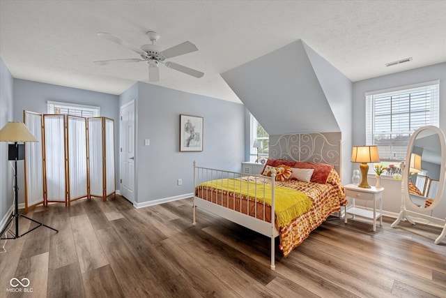 bedroom with a ceiling fan, a textured ceiling, visible vents, wood finished floors, and baseboards
