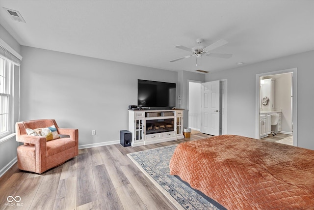 bedroom featuring baseboards, visible vents, a glass covered fireplace, and wood finished floors