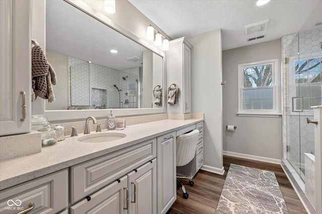 full bathroom featuring vanity, baseboards, wood finished floors, visible vents, and a stall shower