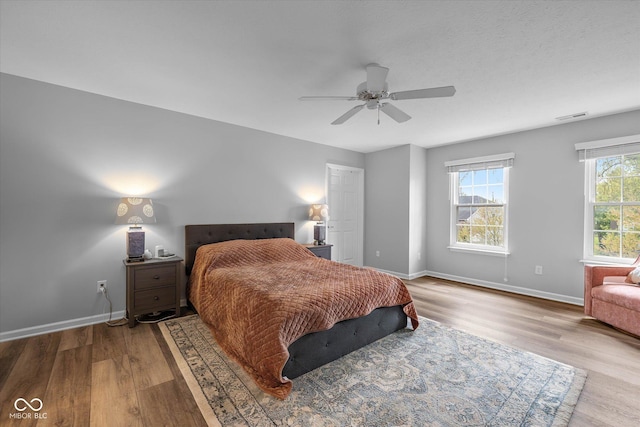 bedroom featuring a ceiling fan, baseboards, visible vents, and wood finished floors