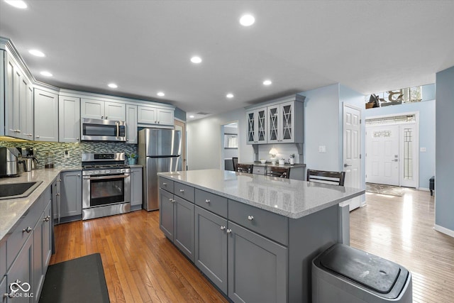 kitchen featuring a kitchen island, tasteful backsplash, light wood-style flooring, gray cabinetry, and stainless steel appliances