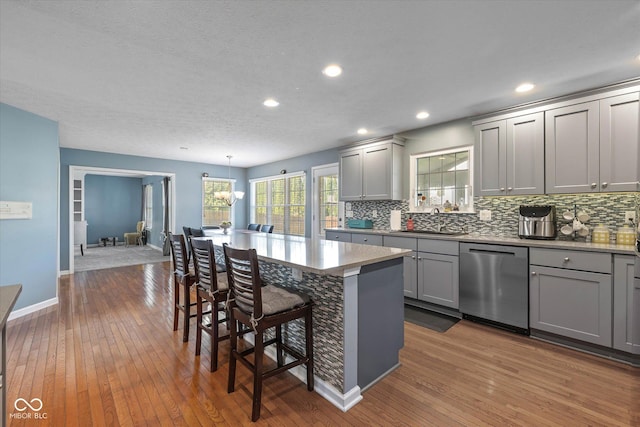 kitchen with stainless steel dishwasher, a sink, backsplash, and gray cabinetry