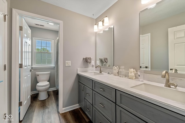 bathroom with a sink, toilet, wood finished floors, and visible vents