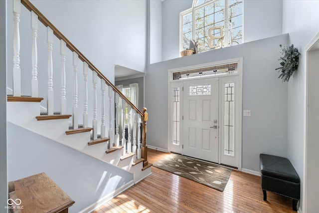 foyer with wood-type flooring, stairs, a towering ceiling, and a healthy amount of sunlight