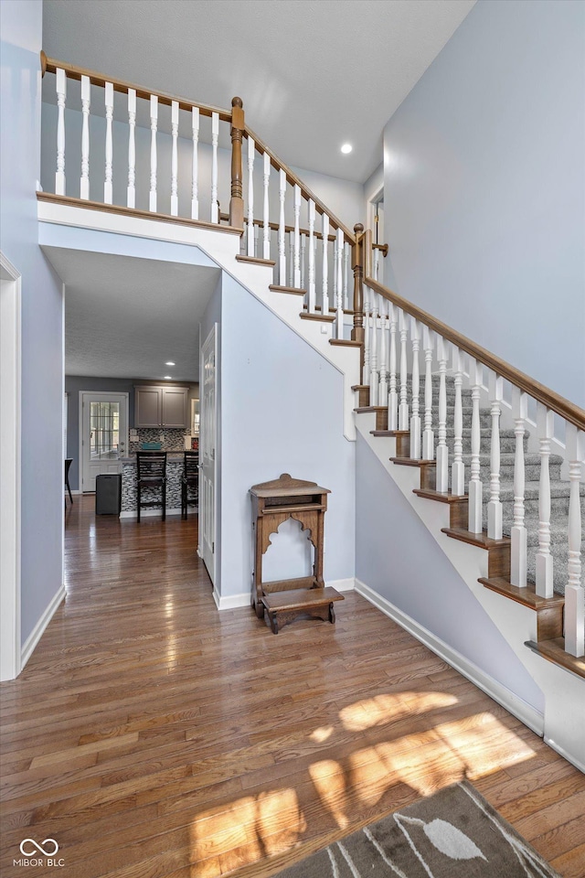stairs with baseboards, a high ceiling, and wood finished floors