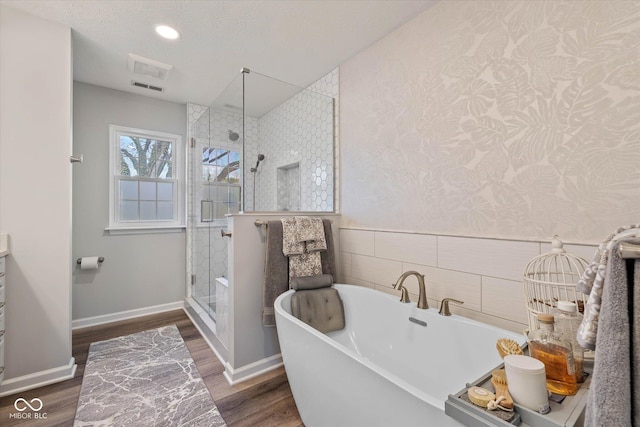 bathroom featuring a freestanding tub, wallpapered walls, a shower stall, wood finished floors, and visible vents
