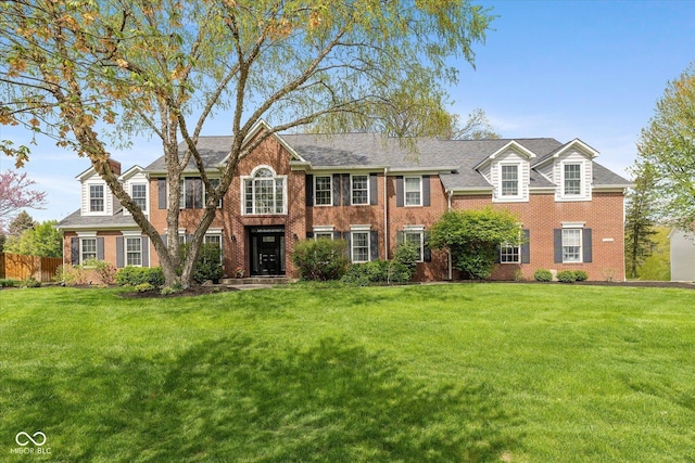 view of front facade featuring brick siding, a front lawn, roof with shingles, and fence