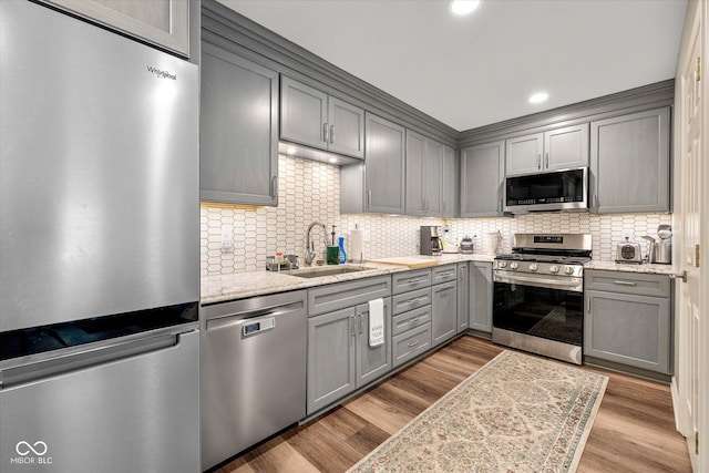 kitchen featuring stainless steel appliances, a sink, decorative backsplash, and gray cabinets