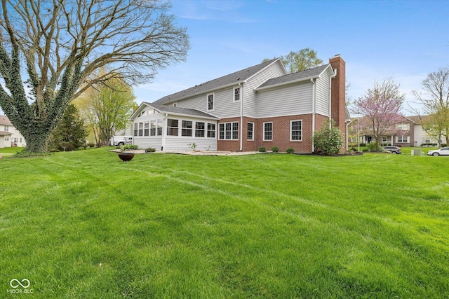 back of house with a lawn, brick siding, a chimney, and a sunroom