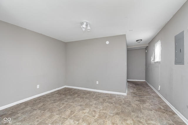 spare room with baseboards, stone finish flooring, and electric panel