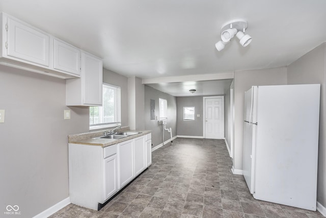 kitchen with a sink, light countertops, freestanding refrigerator, white cabinetry, and baseboards
