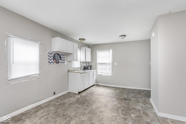 kitchen with baseboards, a sink, white cabinetry, and light countertops