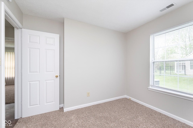 carpeted spare room featuring a healthy amount of sunlight, baseboards, and visible vents