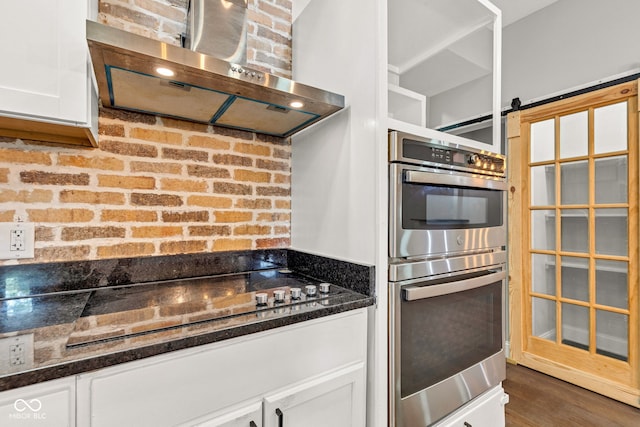 257 N Tacoma Ave, Indianapolis, IN 46201 - kitchen featuring dark stone countertops, wood finished floors, double oven, wall chimney exhaust hood, and white cabinetry